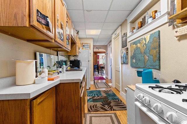 303 N Ashland Ave, Green Bay, WI 54303 - kitchen featuring light wood finished floors, a paneled ceiling, white appliances, brown cabinetry, and light countertops