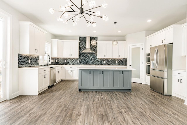 kitchen featuring wall chimney range hood, stainless steel appliances, wood finished floors, and light countertops
