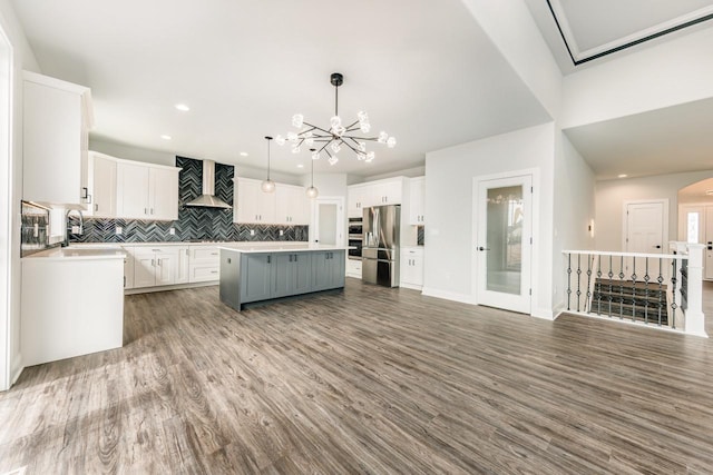 kitchen with a kitchen island, backsplash, freestanding refrigerator, a notable chandelier, and wall chimney exhaust hood