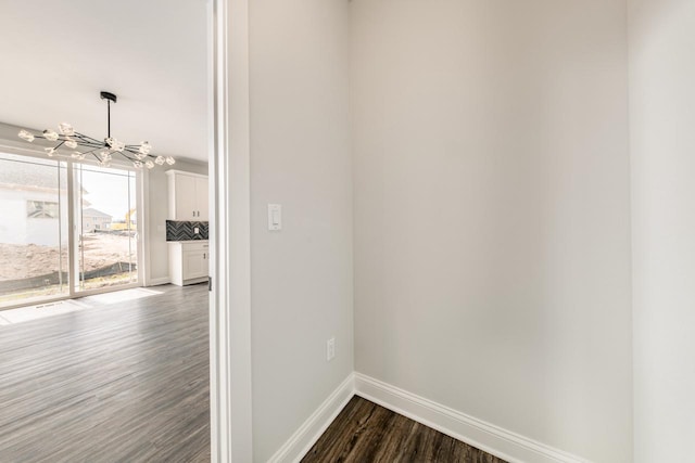 hall featuring baseboards, dark wood finished floors, and a chandelier