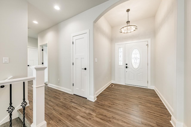 entrance foyer featuring baseboards, arched walkways, dark wood-style flooring, and a chandelier