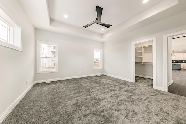 unfurnished bedroom featuring a walk in closet, carpet floors, baseboards, a tray ceiling, and recessed lighting