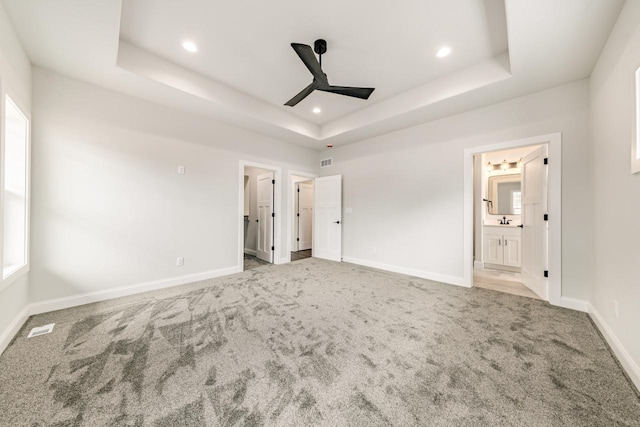 unfurnished bedroom with carpet floors, a tray ceiling, and baseboards