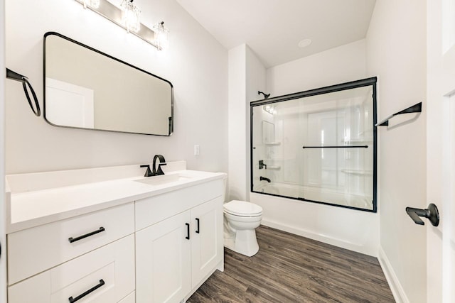 bathroom with vanity, toilet, enclosed tub / shower combo, baseboards, and wood finished floors