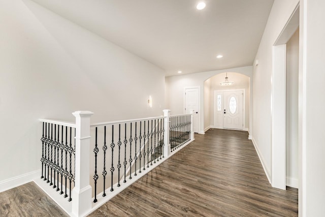 corridor with arched walkways, baseboards, recessed lighting, and wood finished floors