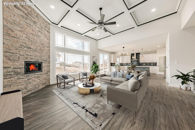 living room featuring a stone fireplace, a towering ceiling, baseboards, ceiling fan with notable chandelier, and coffered ceiling