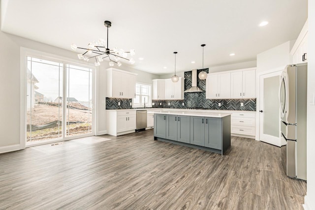 kitchen with wall chimney range hood, an inviting chandelier, gray cabinets, stainless steel appliances, and tasteful backsplash