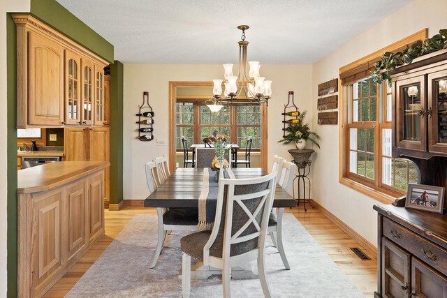 dining space featuring baseboards, an inviting chandelier, visible vents, and light wood-type flooring