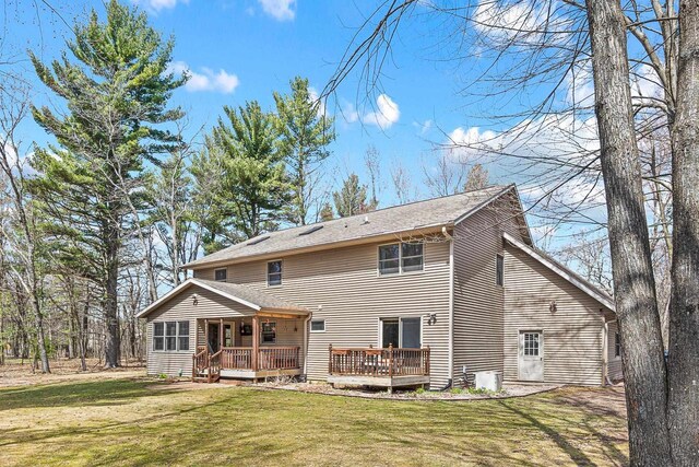 rear view of property with a wooden deck, a lawn, and a shingled roof