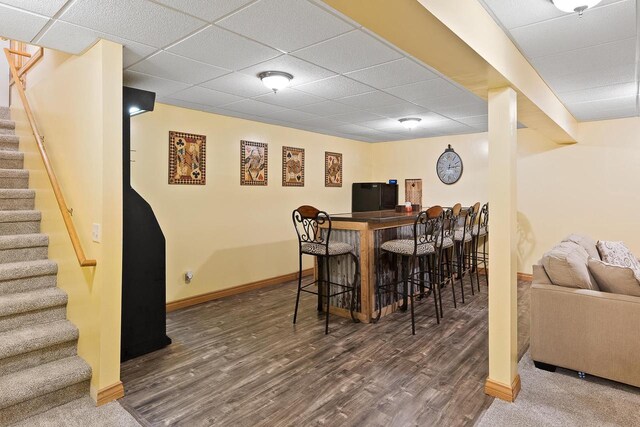 dining space featuring stairway, wood finished floors, a bar, baseboards, and a paneled ceiling