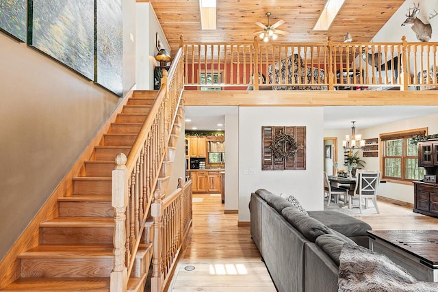 living area with a high ceiling, light wood-style floors, baseboards, wood ceiling, and ceiling fan with notable chandelier