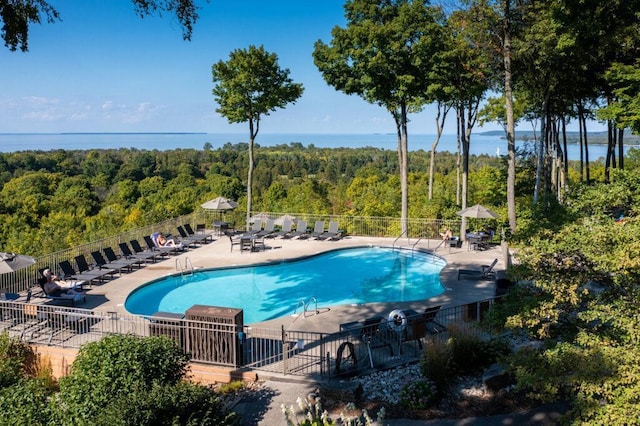 community pool with a forest view, fence, a water view, and a patio