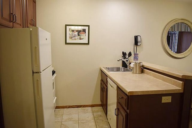 kitchen with a peninsula, a sink, dark brown cabinetry, white appliances, and light countertops