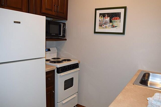 kitchen featuring light countertops, white appliances, dark brown cabinetry, and a sink