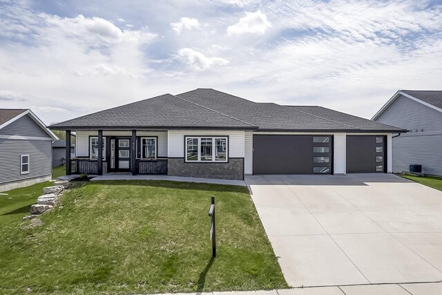 prairie-style house with a garage, covered porch, a front yard, cooling unit, and driveway