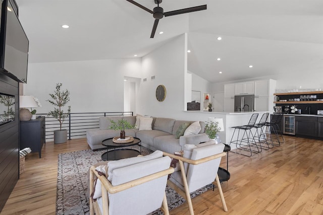 living area featuring light wood-style floors, beverage cooler, ceiling fan, high vaulted ceiling, and bar area