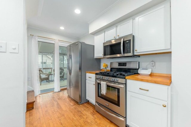 kitchen featuring butcher block counters, appliances with stainless steel finishes, light wood-style flooring, white cabinets, and ornamental molding