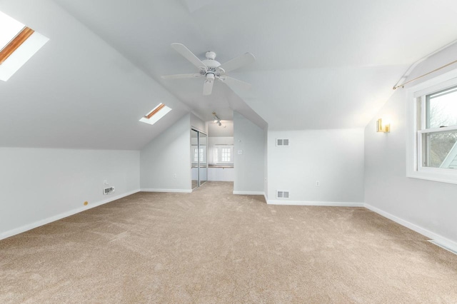 additional living space featuring light carpet, lofted ceiling with skylight, and visible vents