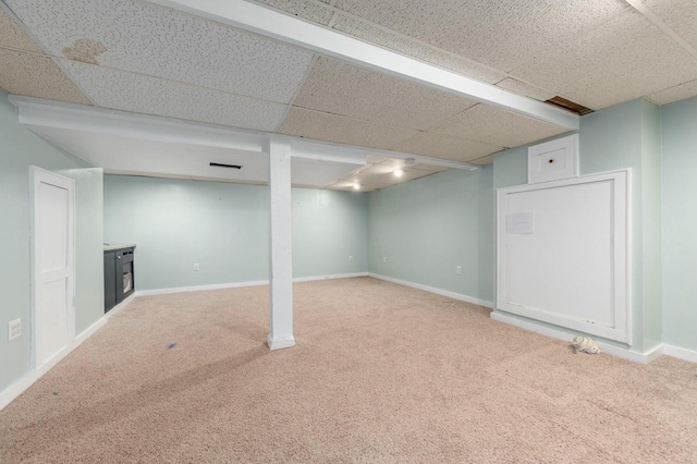 finished basement featuring light carpet, a drop ceiling, and baseboards