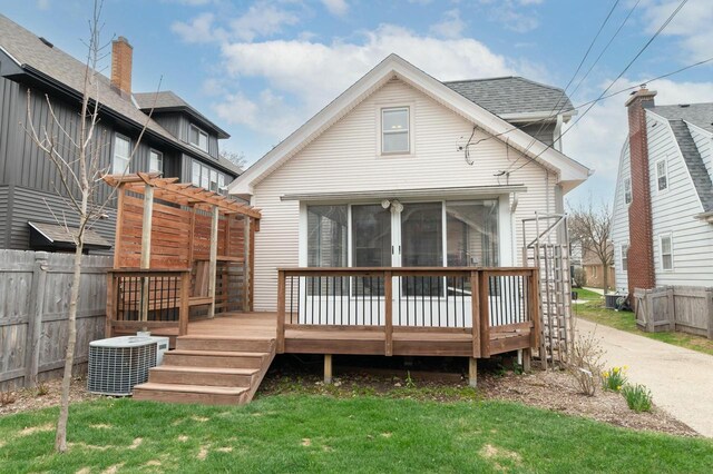 rear view of property with fence, central air condition unit, a wooden deck, a lawn, and a sunroom