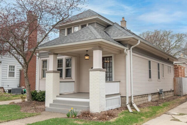 view of front of house featuring a chimney, roof with shingles, central air condition unit, and covered porch