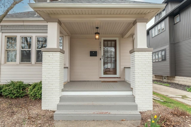 doorway to property with a porch and a shingled roof