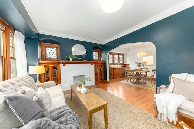 living room featuring a fireplace, wood finished floors, arched walkways, and crown molding