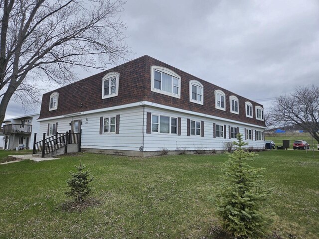 view of front facade featuring a shingled roof, a front yard, and mansard roof