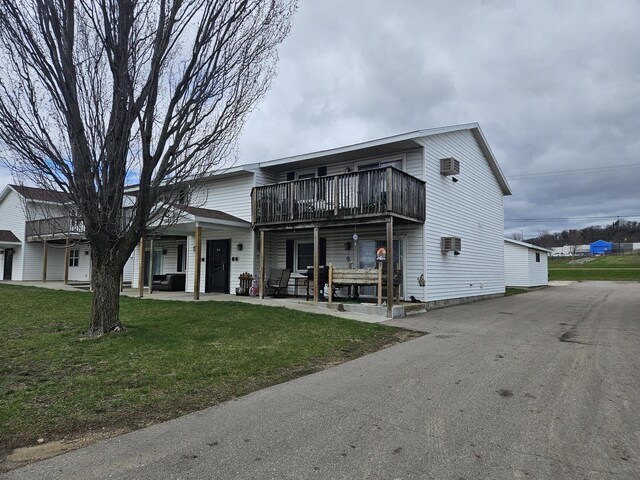 view of front of property featuring a front lawn, a wall mounted air conditioner, a deck, and a patio