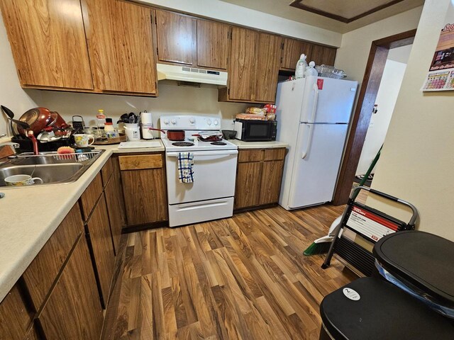 kitchen featuring a sink, wood finished floors, white appliances, light countertops, and under cabinet range hood