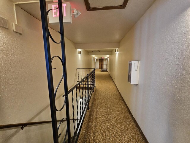 hall featuring a textured wall, carpet flooring, and an upstairs landing