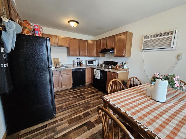 kitchen with a wall mounted air conditioner, under cabinet range hood, light countertops, dark wood-type flooring, and black appliances
