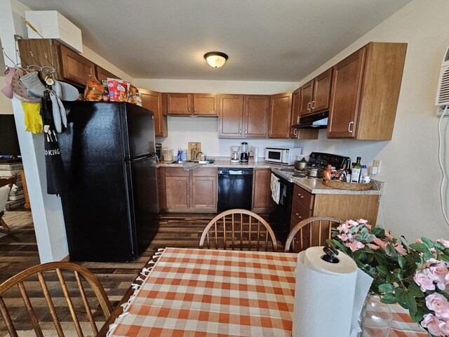 kitchen with dark wood-style floors, under cabinet range hood, light countertops, a sink, and black appliances