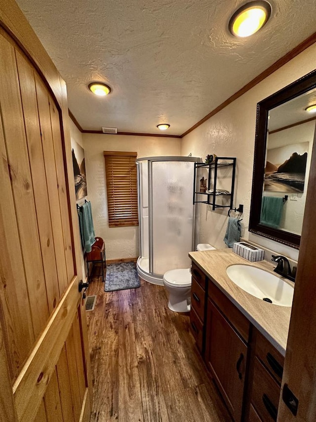 full bathroom featuring a shower stall, wood finished floors, a textured ceiling, vanity, and ornamental molding