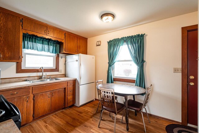 kitchen with brown cabinets, freestanding refrigerator, light wood finished floors, and a sink