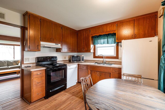 kitchen with a sink, light wood-style floors, white appliances, light countertops, and under cabinet range hood