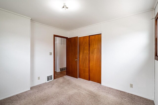 unfurnished bedroom featuring carpet floors, ornamental molding, visible vents, and a closet
