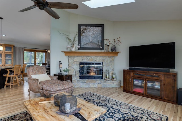 living area featuring a ceiling fan, wood finished floors, and vaulted ceiling with skylight