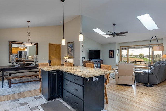 kitchen with ceiling fan, a skylight, light wood-type flooring, light stone counters, and open floor plan