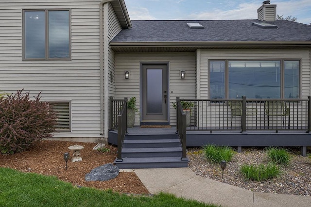 entrance to property featuring a shingled roof, a chimney, and a deck