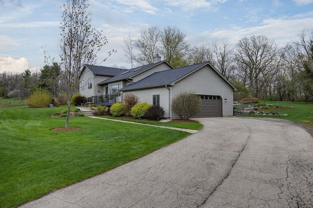 view of side of home featuring a garage, aphalt driveway, a chimney, a shingled roof, and a lawn