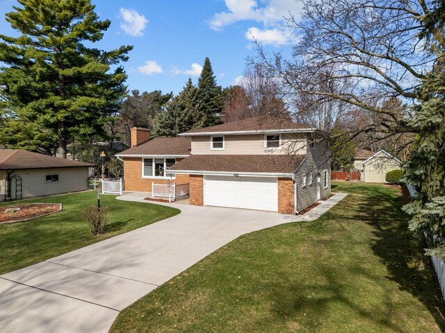 1442 Traeger St, Green Bay, WI 54304 - split level home featuring concrete driveway, a chimney, a front lawn, an attached garage, and brick siding