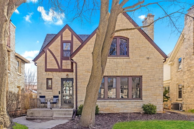 back of house featuring a chimney, central AC unit, roof with shingles, and stone siding