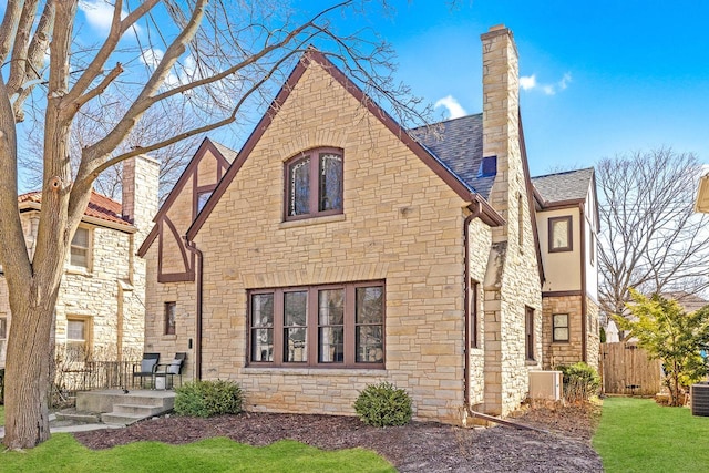 rear view of house with a shingled roof, fence, a chimney, and stone siding