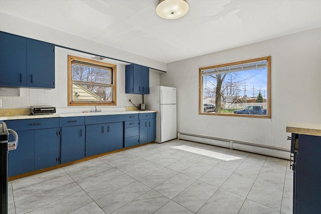 kitchen with backsplash, a healthy amount of sunlight, a baseboard heating unit, freestanding refrigerator, and blue cabinetry