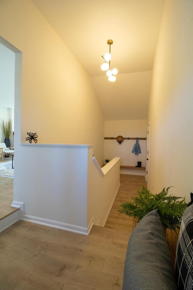 hallway with vaulted ceiling, light wood-type flooring, an inviting chandelier, and an upstairs landing