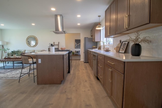 kitchen with wall chimney exhaust hood, light countertops, a breakfast bar, a kitchen island, and appliances with stainless steel finishes