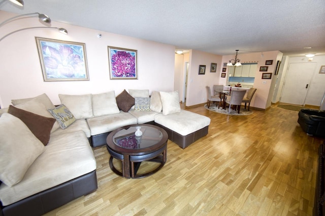 living room featuring light wood-style floors, a textured ceiling, baseboards, and a notable chandelier