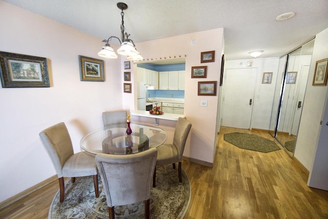 dining area with baseboards, a chandelier, wood finished floors, and a textured ceiling