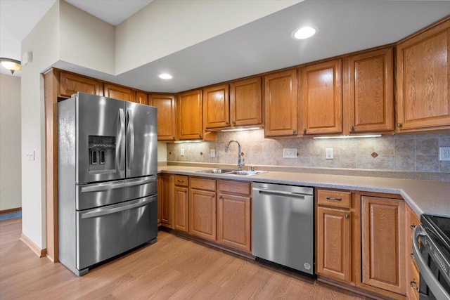 kitchen with appliances with stainless steel finishes, brown cabinets, light wood-type flooring, and a sink